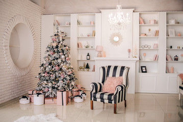 Christmas interior in pastel pink, white and black colors. Fireplace, armchair, Christmas tree and many gifts. Stylish, luxurious apartment decor.