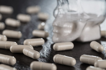 Close-up pile of white color medical pills on against a glass skull with white powder