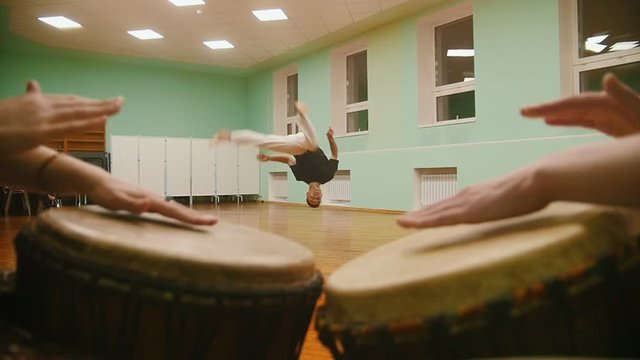 Fighter performs martial tricks with dance elements on background playing a two musical instruments jembe