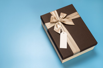 Gift box with a blank label attached on a blue background with copy space. Festive background.