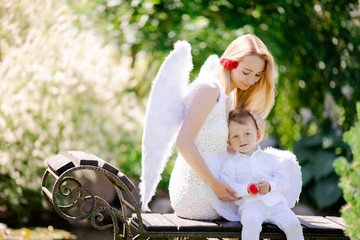 Beautiful mother and her toddler son wearing angel costumes. Cheerful moment, loving family.