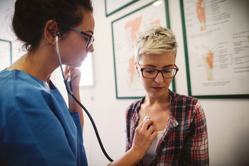 Female middle-aged doctor using stethoscope to examine patient.