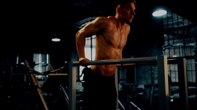 fitness, sport, bodybuilding and people concept - young man doing triceps dip exercise on parallel bars in dark gym