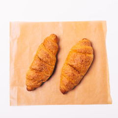 Close-up two cooked croissants on brown baking paper