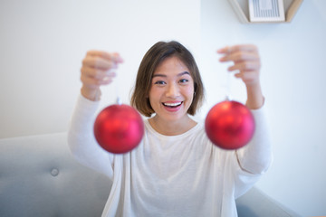 Cheerful young Asian woman giving Christmas balls to you. Happy excited pretty woman decorating tree. Christmas tradition concept