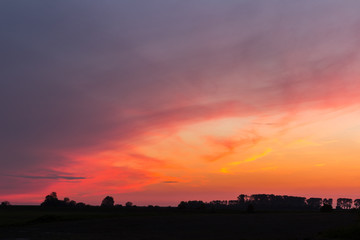 Natural Sunset Sunrise Over Field Or Meadow. Bright Dramatic Sky And Dark Ground. Countryside Landscape Under Scenic Colorful Sky At Sunset Dawn Sunrise. Sun Over Skyline, Horizon. Warm Colours.