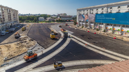 Asphalt paver, roller and truck on the road repair site during asphalting timelapse. Road construction equipment.