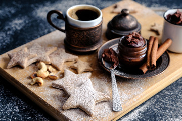 A beautiful Christmas still life of hot black coffee, homemade stars-shaped cookies, cinnamon sticks, flour and sugar sprinkles
