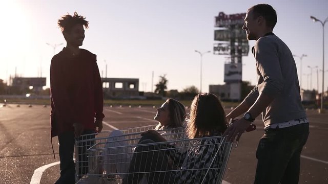 Young friends having fun on a shopping carts. Multiethnic young people playing with shopping cart. Malefriends standing near the shopping corts with their girlfriends. Outdoors