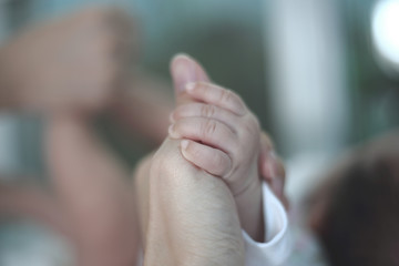 baby's hand holding adult finger while someone changing her diaper in the blured background. Giving support and comfort to a baby.