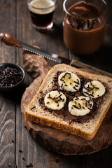 Delicious open sandwich with chocolate and banana on old wooden board and dark table. Breakfast background.