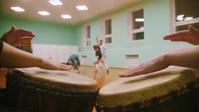Playing a two musical instruments jembe or atabaque on background male fighter performs martial tricks with dance elements in the sport gym