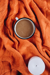 Winter or autumn cozy concept. Cup of coffee and candle on orange knitted sweater. Flat lay, top view.	