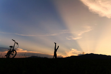 Silhouette of happy child playing upside down outdoors in summer park walking on hands at sunset