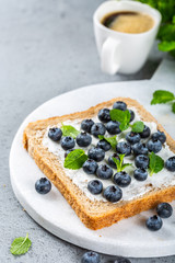Delicious open sandwich with goat cheese and blueberries for breakfast or lunch on marble board. Food background with copy space.