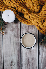 Cup of coffee  with milk, candle, bumps, spruce branches and warm orange scarf on wooden table.Winter concept. Flat lay, top view. 