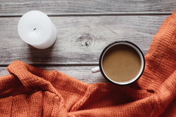 Winter cozy concept. Flat lay of orange knitted sweater, candle and coffee with milk  on wooden table