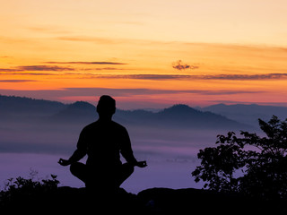 Silhouette of man doing yoga on top mountain at sunset or sunrise time
