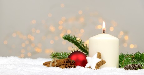 Christmas background - candle with pine branches and spices in the snow with blurred lights in the background