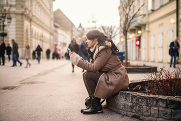 Gorgeous Caucasian woman sitting and writing or reading message on cold weather. Warm clothes on.