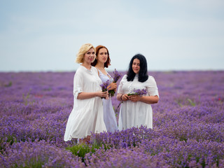 Three young girls with different hair color in white dresses, posing together in a lavender field.