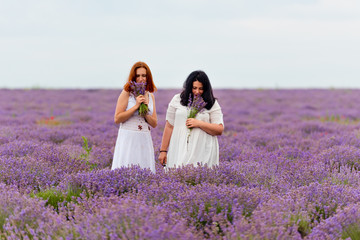 Two young girls with different hair color in white dresses, posing together in a lavender field.