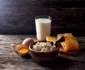 Milk in glass, honeycomb and eggs on a wooden background. Cottage cheese in a wooden bowl, rustic style. Dairy products in the morning for breakfast are very healthy.