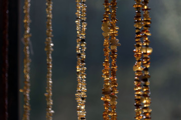 Beads from amber hang parallel to each other on a blurred background. Some. Day. Sunlight makes amber magical, glowing from the inside.