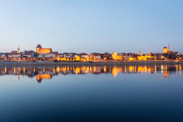 Fototapeta na wymiar TORUN, POLAND - panorama of the Old Town district, listed as one of UNESCO World Heritage Sites, with picturesque night illuminations and evening sky water reflections.
