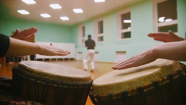 Playing a two musical instruments jembe on background male fighter performs martial tricks with dance elements