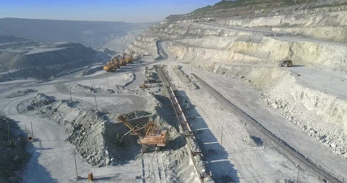 big power shovel loads ore train with asbes in huge quarry