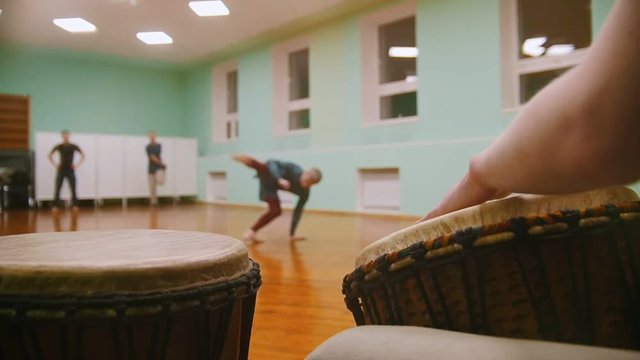 Playing a musical instruments jembe or atabaque on background male fighter performs martial tricks with dance elements