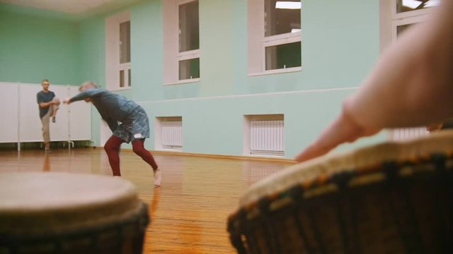 male fighter performs martial tricks with dance elements on background playing a two musical instruments jembe or atabaque