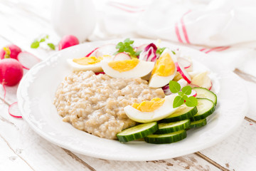 Oatmeal porridge with boiled egg and vegetable salad with fresh radish, cucumber and lettuce. Healthy dietary breakfast