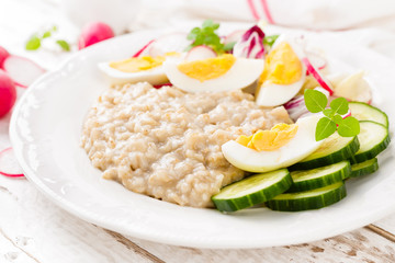 Oatmeal porridge with boiled egg and vegetable salad with fresh radish, cucumber and lettuce. Healthy dietary breakfast