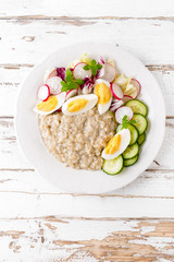 Oatmeal porridge with boiled egg and vegetable salad with fresh radish, cucumber and lettuce. Healthy dietary breakfast