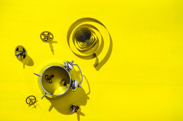 Old alarm clock disassembled into gears on a bright yellow background with hard shadows.