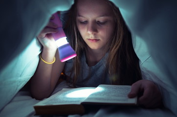Young girl reading a book in bed