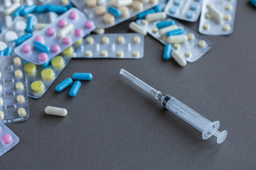 Fototapeta na wymiar Syringe with assorted pharmaceutical packaging of tablets and pills on gray background
