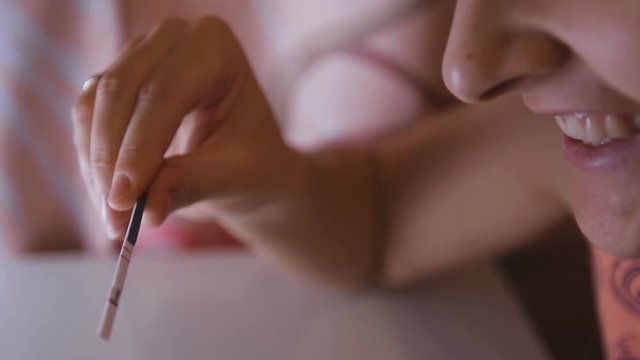 A young happy woman holds a positive pregnancy test in her hand and smiles.