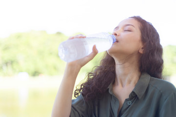 Young Asian female drinking water with a plastic bottle in her hand on nature. clean water are good for health and recovery concept