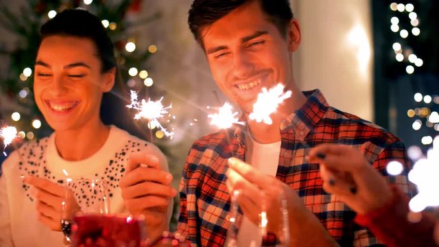 holidays and celebration concept - happy friends with sparklers having christmas dinner party or celebrating new year at home