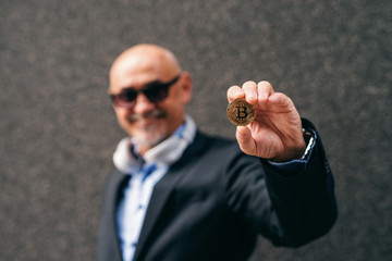 Fototapeta premium Bearded senior adult wealthy businessman holding bit-coin. Selective focus on bit-coin.