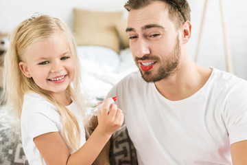 happy father and cute little daughter playing and applying makeup at home