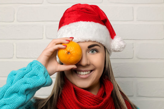 girl in a santa claus hat is holding tangerines in front of her face in her hands on a light background. new Year. Christmas