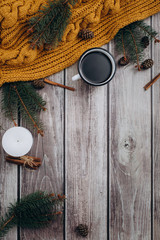 Cup of coffee  , candle, bumps, cinnamon, spruce branches and warm orange scarf on wooden table. Winter concept. Flat lay, top view. 