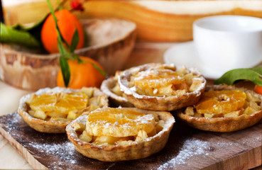 Naklejka na ściany i meble Apple and Orange Tarts , decorated powdered sugar, on wooden board. A simple tart topped with buttery soft apples, orange slice and sugar powder