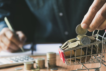 Hand holding a coin with pile of coin in the shopping cart for accounting and business concept.