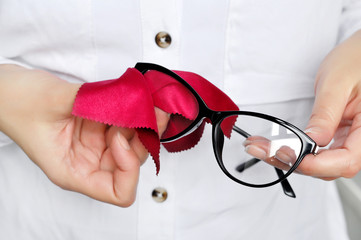 Women hand cleaning trendy black glasses lens with red microfiber tissue.healthcare, vision and medicine concept 