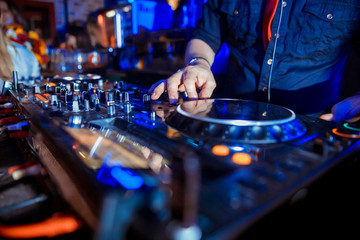 Dj mixes the track in the nightclub at party. Headphones in foreground and DJ hands in motion
